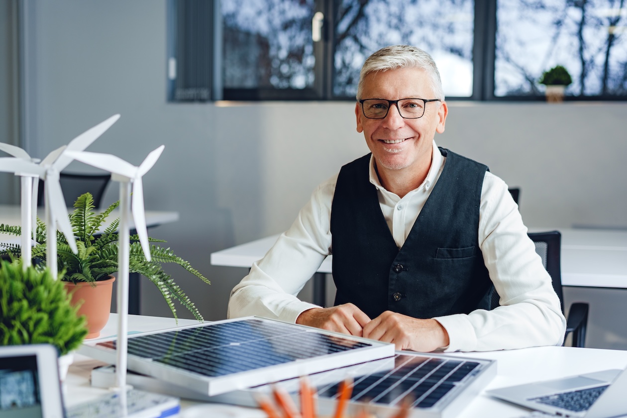 A senior engineer at his desk with wind turbine and solar panel models